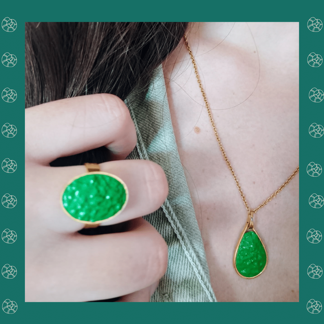 main portant une bague verte et un pendentif assorti